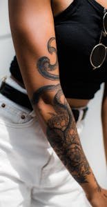 Close-up of a woman's tattooed arm with snake and floral design. Perfect for fashion and lifestyle themes.