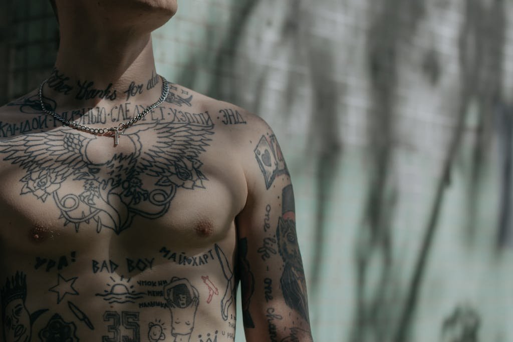 Detailed close-up of a tattooed male torso with varied designs, captured in soft shadowed lighting.