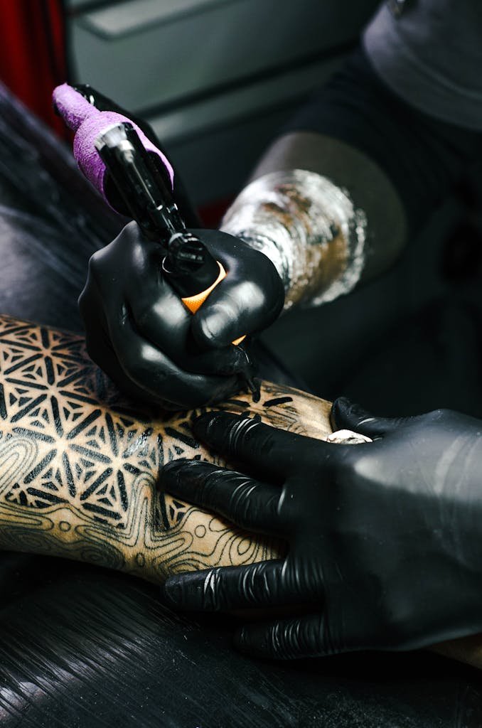 Tattoo artist working on intricate black and white design indoors.